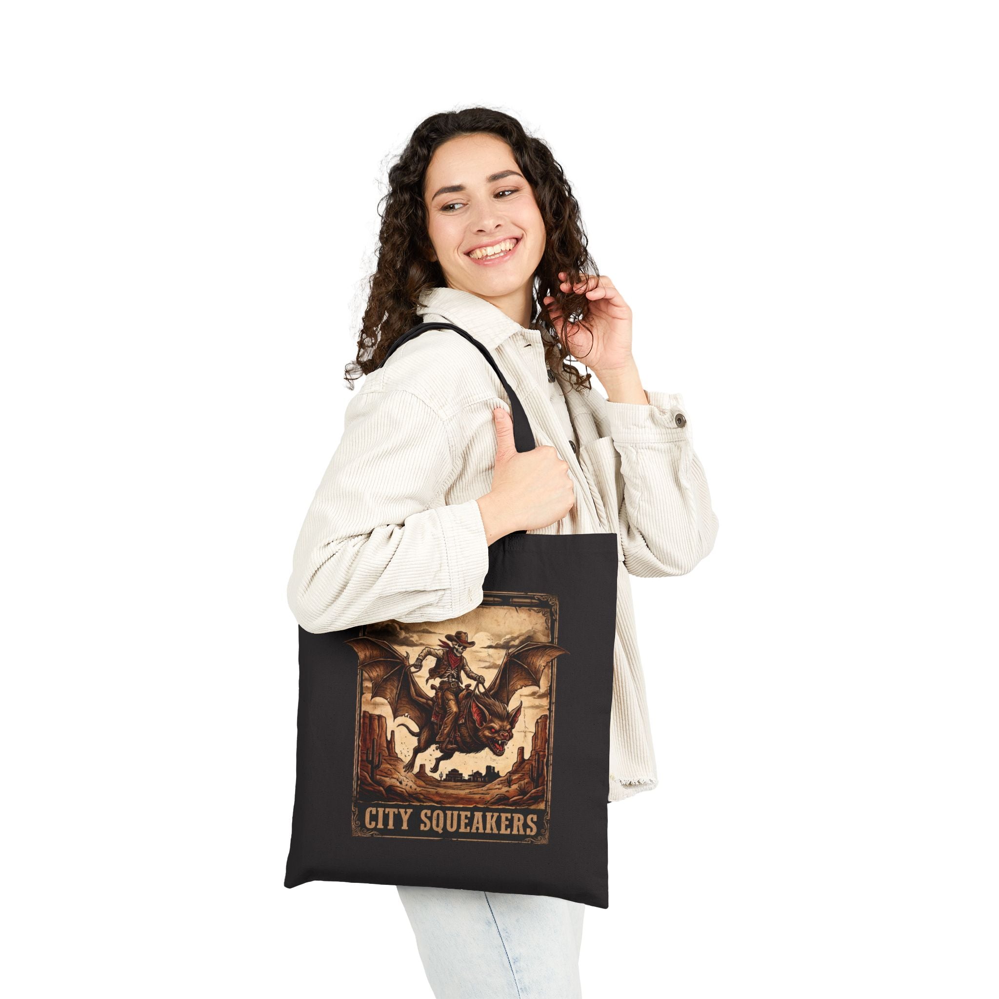 Woman holding black City Squeakers  tote bag side view — vintage skeleton cowboy bat rider graphic, heavy cotton shoulder bag for everyday carry