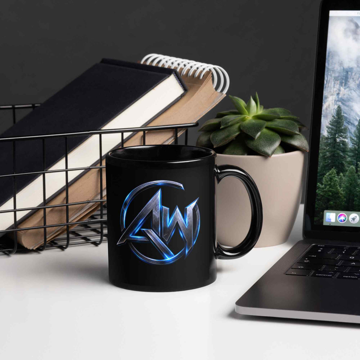 Black mug with a AW logo on a desk with a laptop, books, and plant