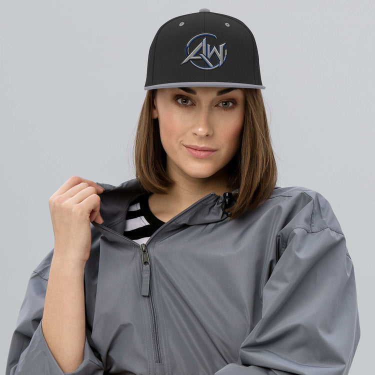 Woman wearing a gray raincoat and black  and  silver hat with AW logo on a gray background