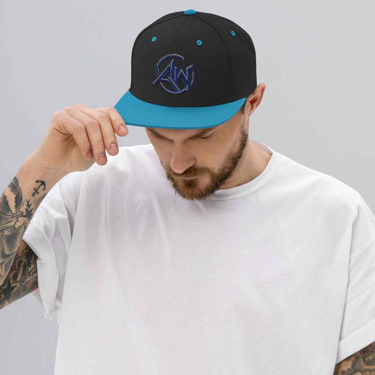 A man wearing a black snapback cap with a bright blue visor and blue embroidered AW logo, paired with a white t-shirt, against a plain light gray background.