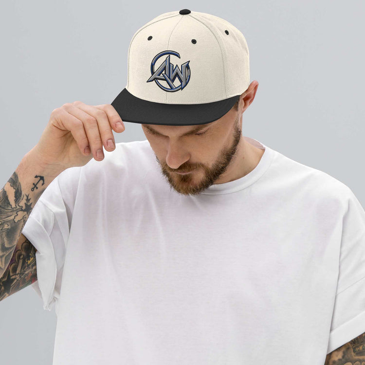 A man wearing a cream and black snapback cap with a stylized 'AW' logo on the front, paired with a white t-shirt, set against a solid gray background.
