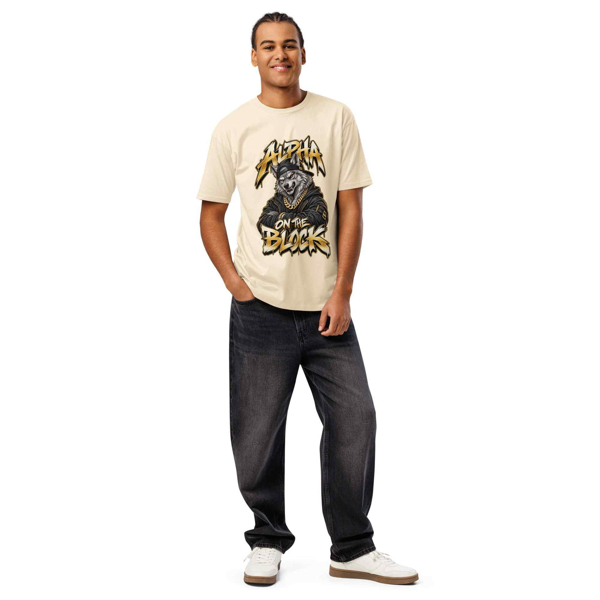 A man modeling a cream-colored graphic t-shirt with a wolf and 'ALPHA ON THE BLOCK' text, paired with dark gray jeans and white sneakers, against a plain white background.