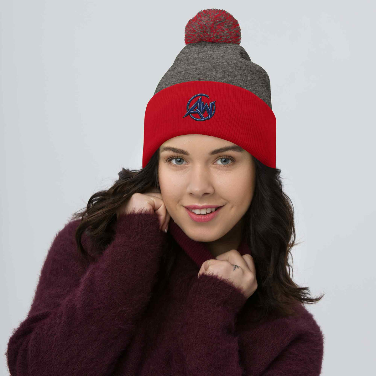 Woman wearing a red and gray beanie with a pom-pom on a plain background