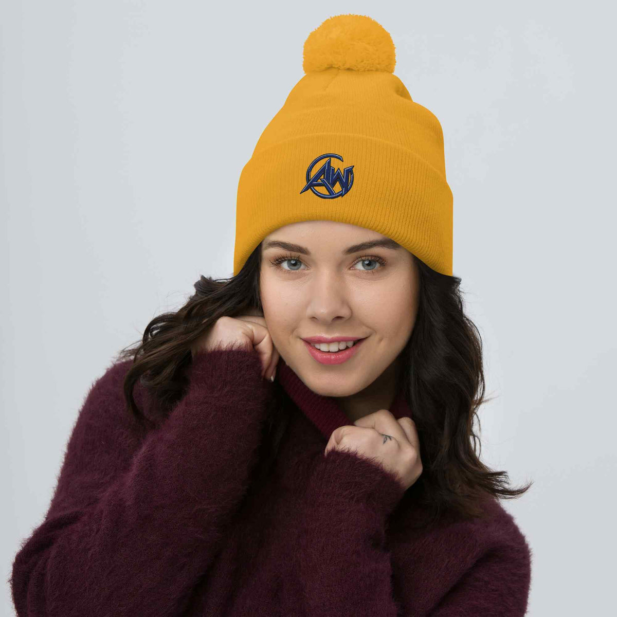 Woman wearing a yellow beanie with blue AW design on a plain background
