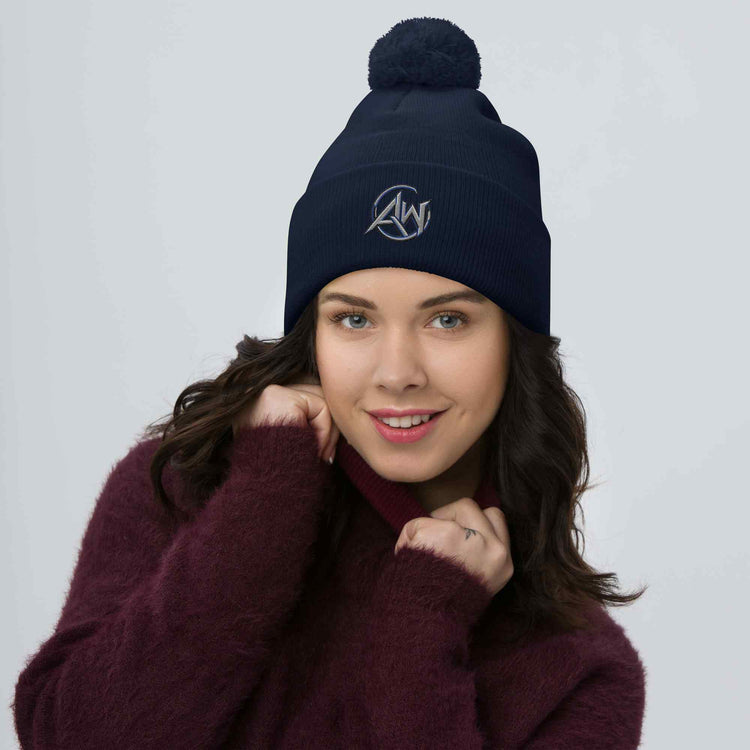 Woman wearing a navy blue beanie pom pom  with an AW  logo on a light gray background