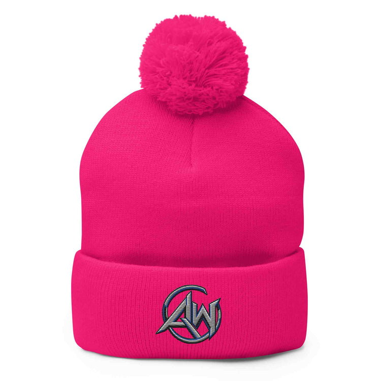 A bright pink knit beanie with a fluffy pom-pom on top and a folded cuff featuring a gray embroidered circular logo with the letters AW