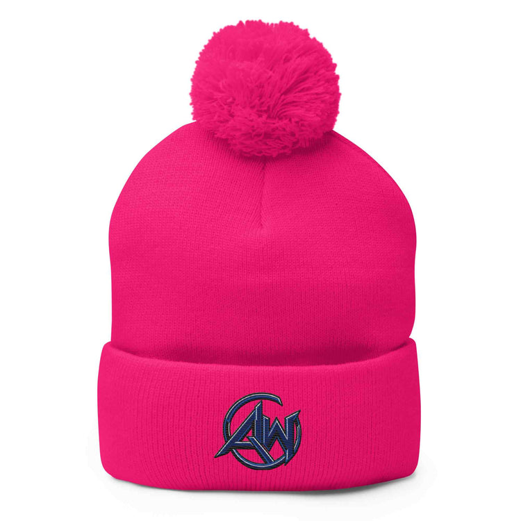 A bright pink knit beanie with a fluffy pom-pom on top and a folded cuff featuring a dark navy embroidered circular  AW logo with stylized letters, shown on a plain white background.