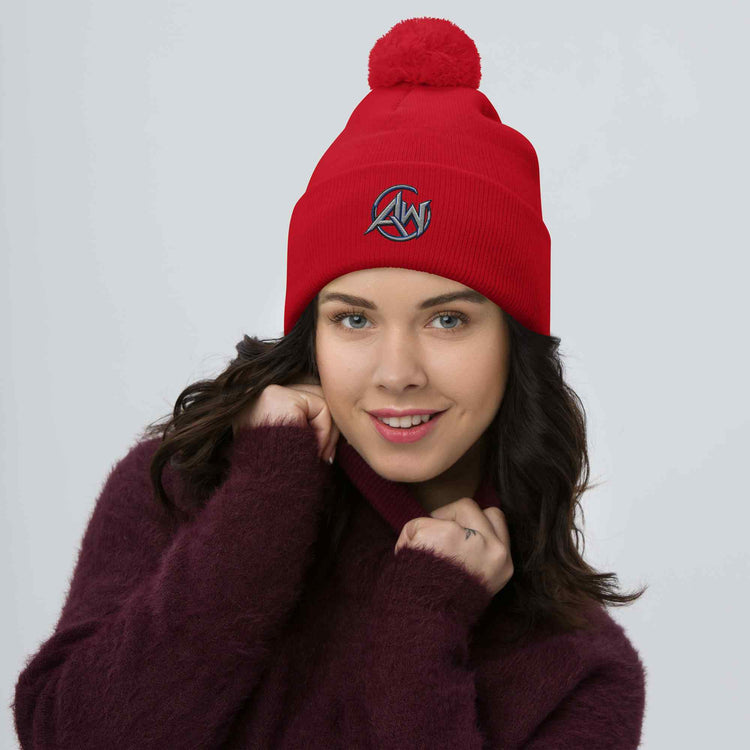 Woman wearing a red knit beanie pom pom  with an AW logo design on a plain background