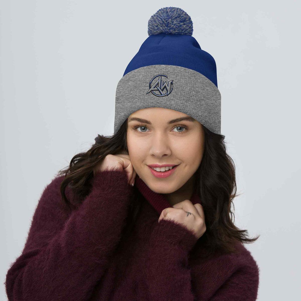 Woman wearing a two-toned beanie pom pom  with a gray and blue AW  design on a white background