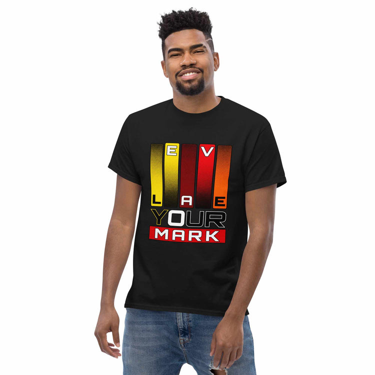 A man wearing a black short-sleeve t-shirt with a colorful graphic that spells out 'LEAVE YOUR MARK' using vertical stripes in yellow, orange, and red, paired with blue jeans, against a plain white background.