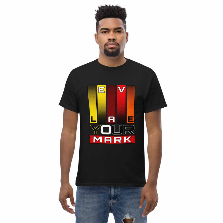 A man wearing a black short-sleeve t-shirt with a colorful graphic on the chest that reads 'LEAVE YOUR MARK' in yellow, red, orange, and white, paired with blue jeans, against a plain white background.