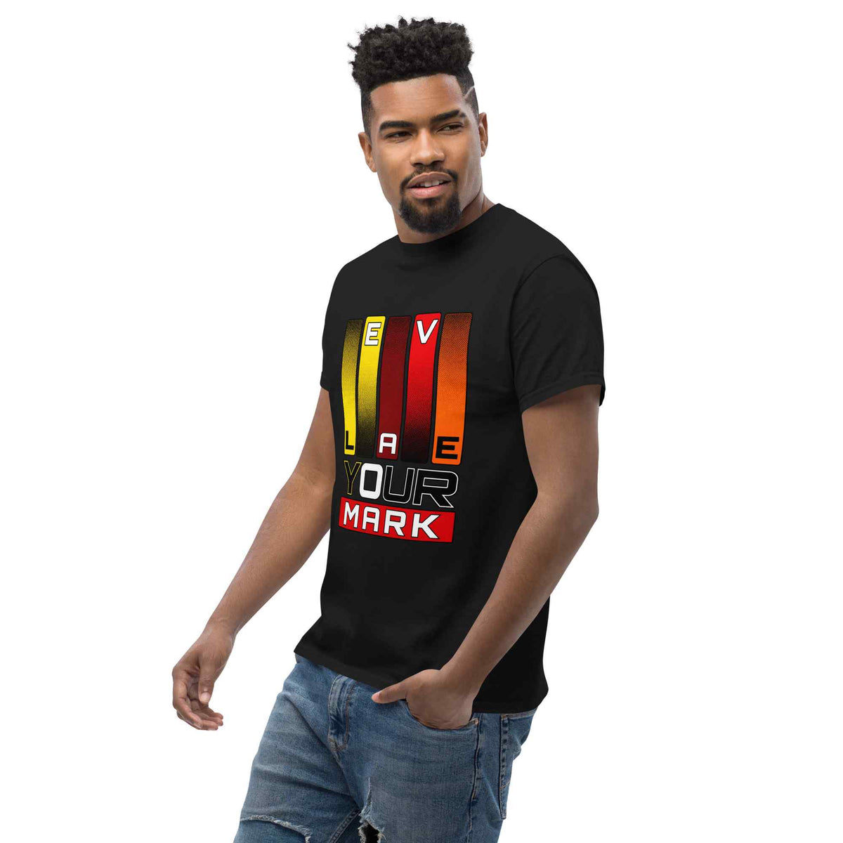 A man wearing a black short-sleeve t-shirt with a colorful graphic print that reads 'YOUR MARK' over vertical yellow, orange, and red stripes, paired with blue jeans, on a solid white background.