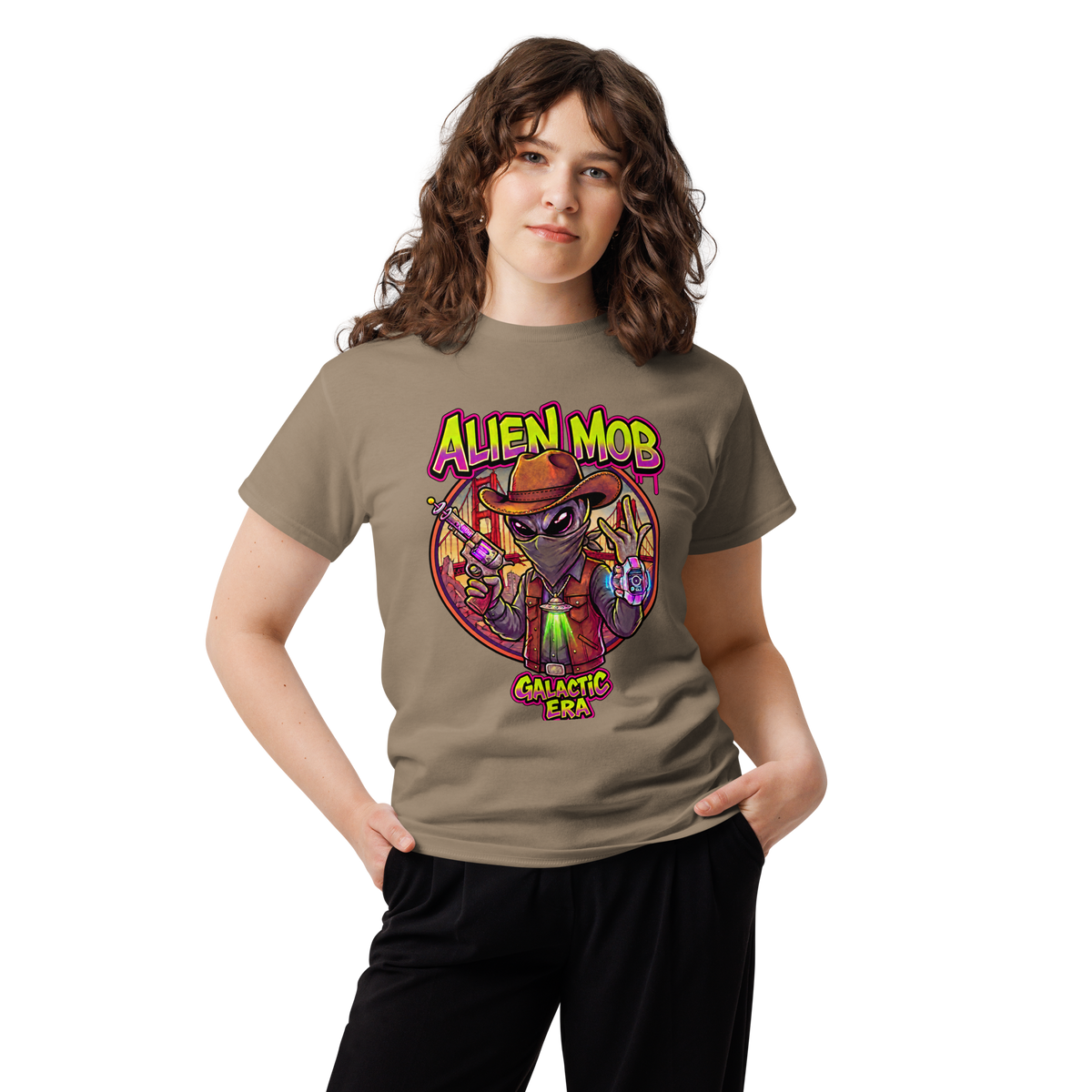 A woman modeling a savana brown t-shirt with a colorful graphic of an alien wearing a cowboy hat and vest, with the text 'ALIEN MOB' and 'GALACTIC ERA'.