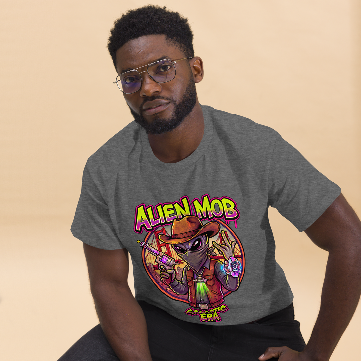 A man wearing a heather gray t-shirt with a colorful cartoon alien graphic that reads 'ALIEN MOB' GALACTIC ERA'.