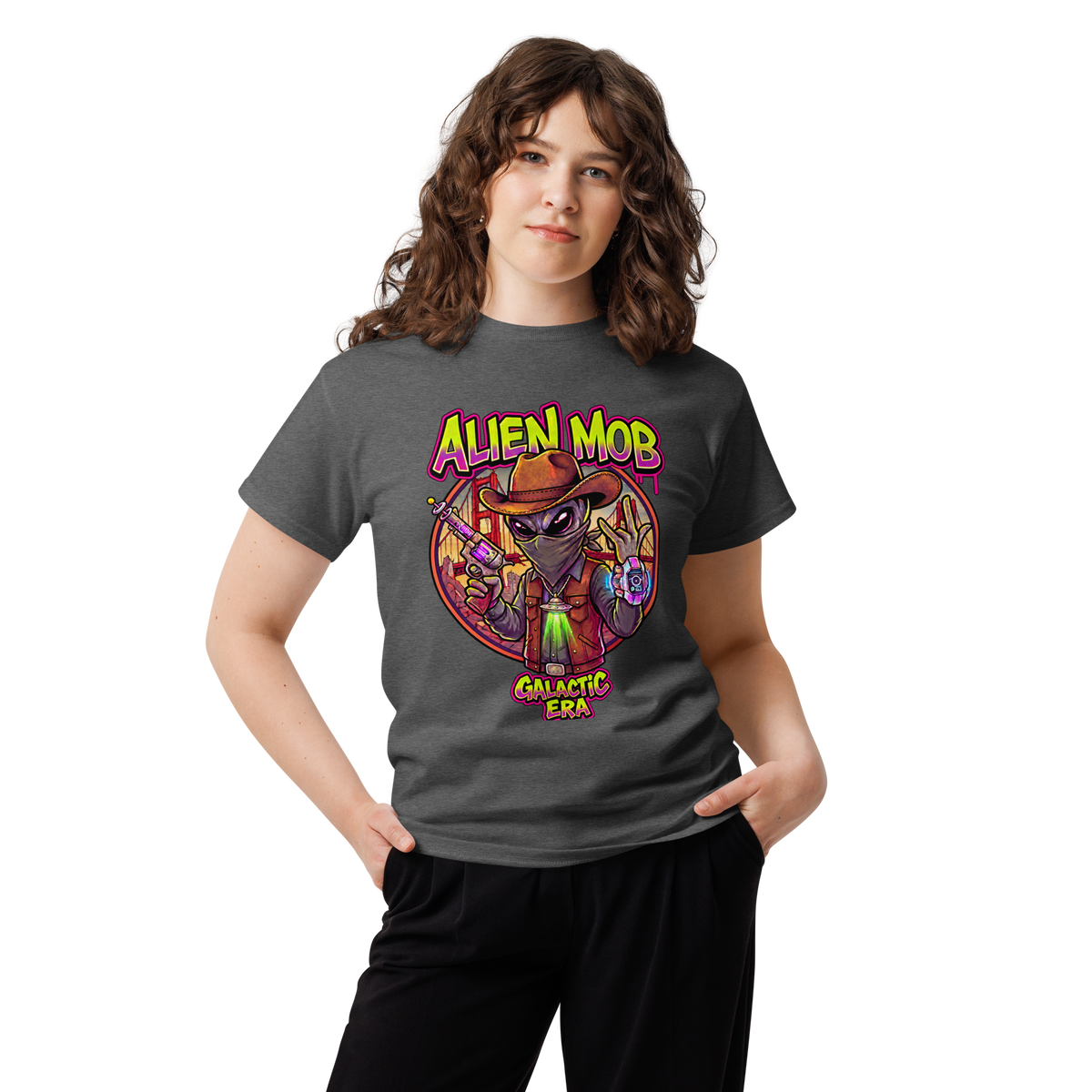 A young woman with wavy brown hair wearing a dark gray graphic  Alien mob galactic ERA' t-shirt and black sweatpants, standing against a plain white background.