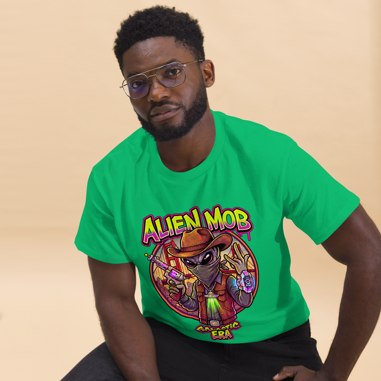 A man wearing a bright green t-shirt with a colorful cartoon alien graphic that reads 'ALIEN MOB' and 'GALACTIC ERA', posed against a solid beige background.