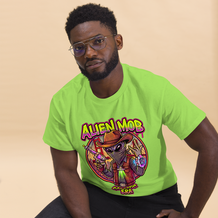 A man wearing a bright lime green t-shirt with a colorful cartoon alien graphic that reads 'ALIEN MOB'  ERA', posed against a solid beige background.