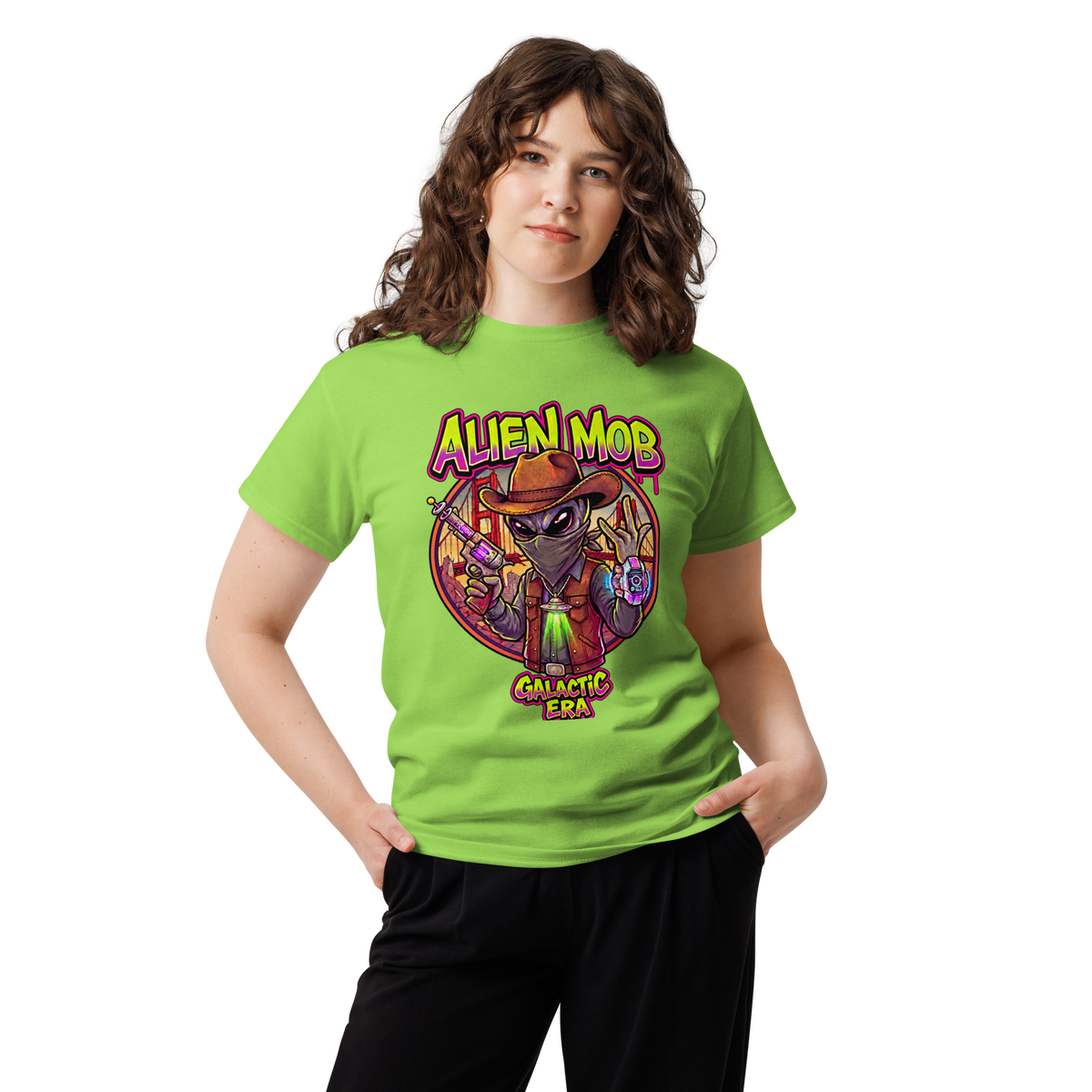 A woman modeling a bright lime green t-shirt with a colorful graphic print of an alien wearing a cowboy hat and the text 'ALIEN MOB GALACTIC ERA'.