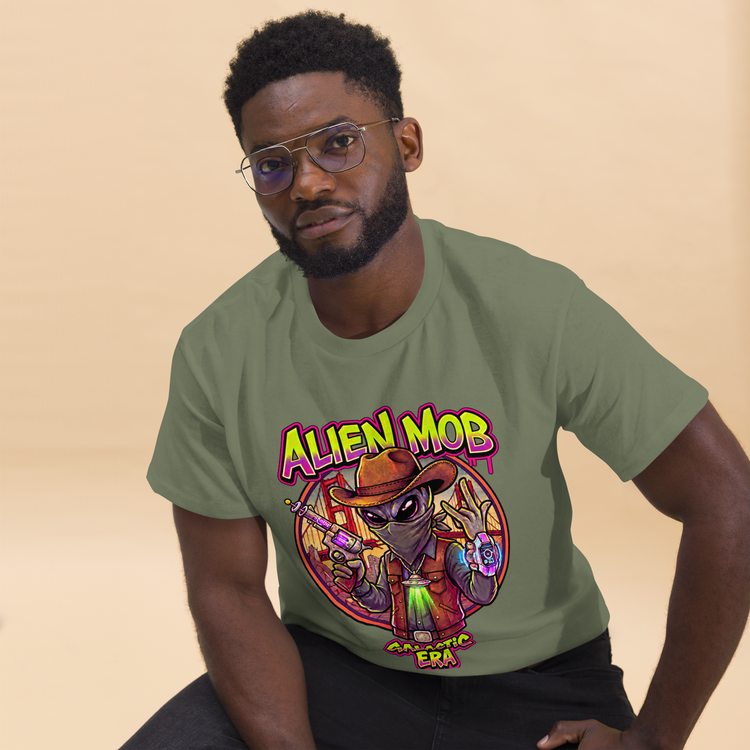  A man wearing a Military Green  Tee With a graphic print on Alien Character cowboy outlaw Text Alien MOB  GALATIC ERA 