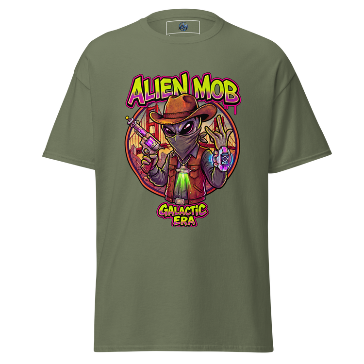 An olive green short-sleeve t-shirt with a colorful graphic print on the front. The graphic features a cartoon alien wearing a brown hat and vest, holding a purple device, with the text 'ALIEN MOB' above and 'GALACTIC ERA' below.