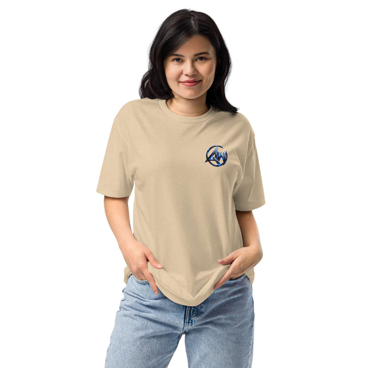 A woman modeling a beige crewneck t-shirt with a small blue circular logo AW text graphic on the left chest, paired with light blue jeans, against a plain white background.