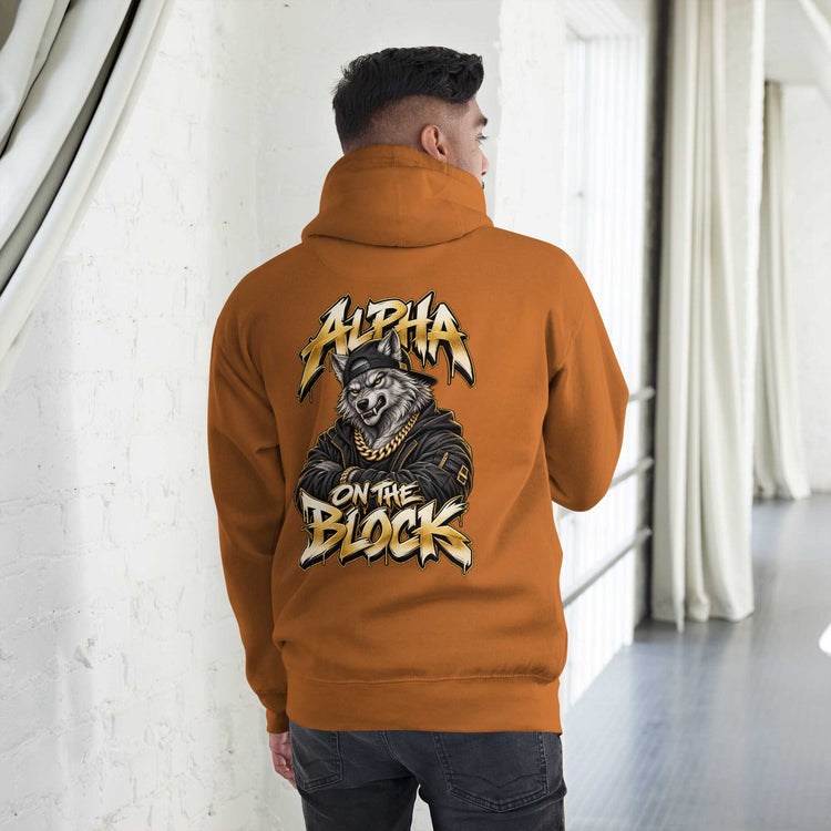 A man viewed from behind wearing an orange hoodie with a large graphic on the back. The graphic features a wolf wearing a cap and sunglasses, a gold chain, and the text 'ALPHA ON THE BLOCK' in a stylized yellow and white font.