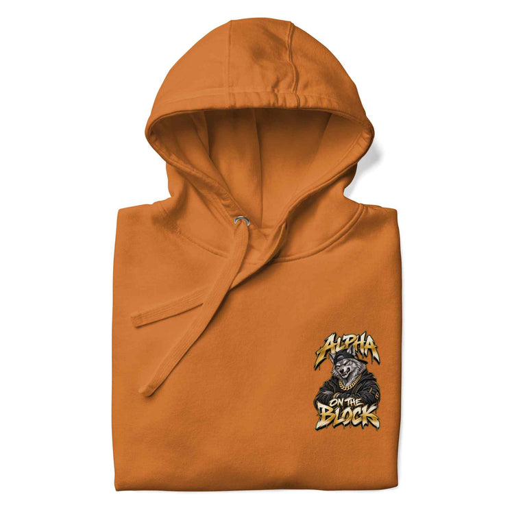 An orange hooded sweatshirt, folded and shown flat against a white background, featuring a graphic on the lower right that reads 'Alpha On The Block' with a wolf illustration.