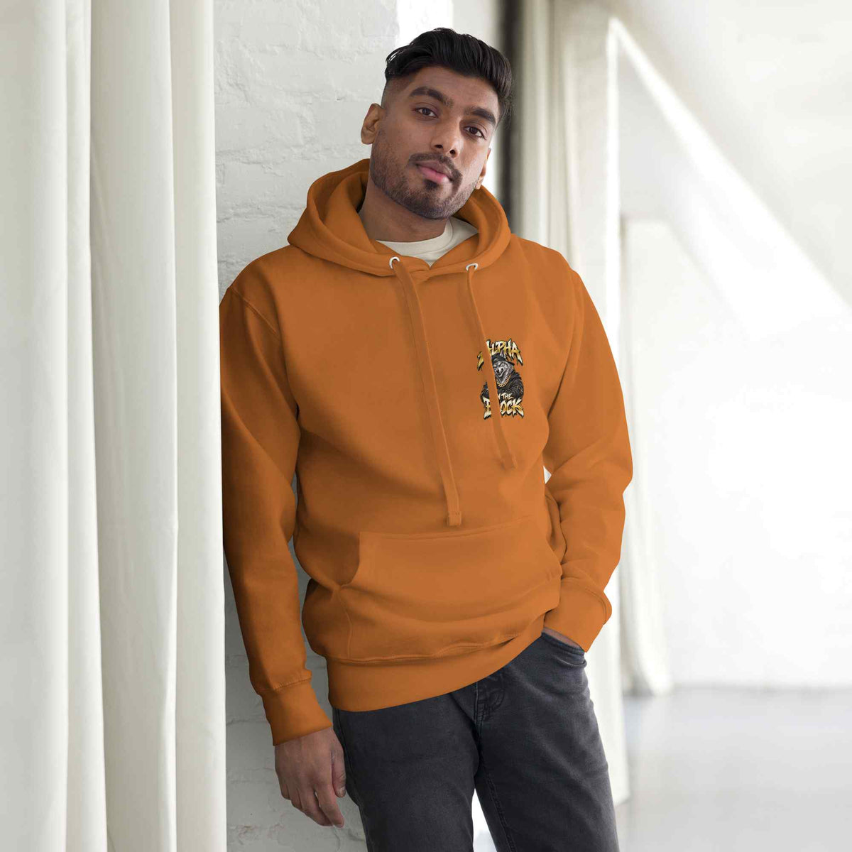 Man wearing an orange hoodie leaning against a white wall.