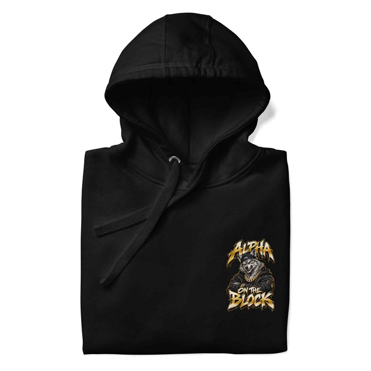 A folded black hoodie with a drawstring hood, featuring a graphic print on the left chest of a wolf wearing a gold hood and the text 'ALPHA ON THE BLOCK' in a stylized gold font, shown on a plain white background.