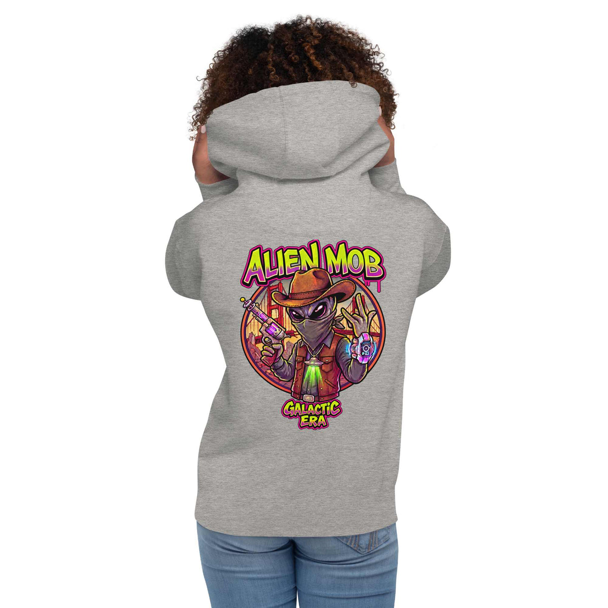 woman wearing a Carbon stone gray hoodie with alien mob cowboy outlaw  on the back of the hoodie paired with blue jeans on a white background back view