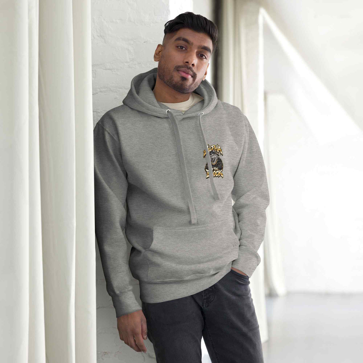 Man wearing a gray hoodie with a logo and text, standing against a white wall.