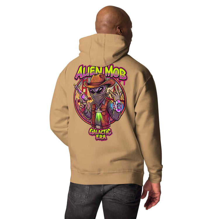 man wearing a khaki hoodie with custom design alien mob cowboy outlaw print on the back of pullover hoodie paired with black jeans on a white background back view