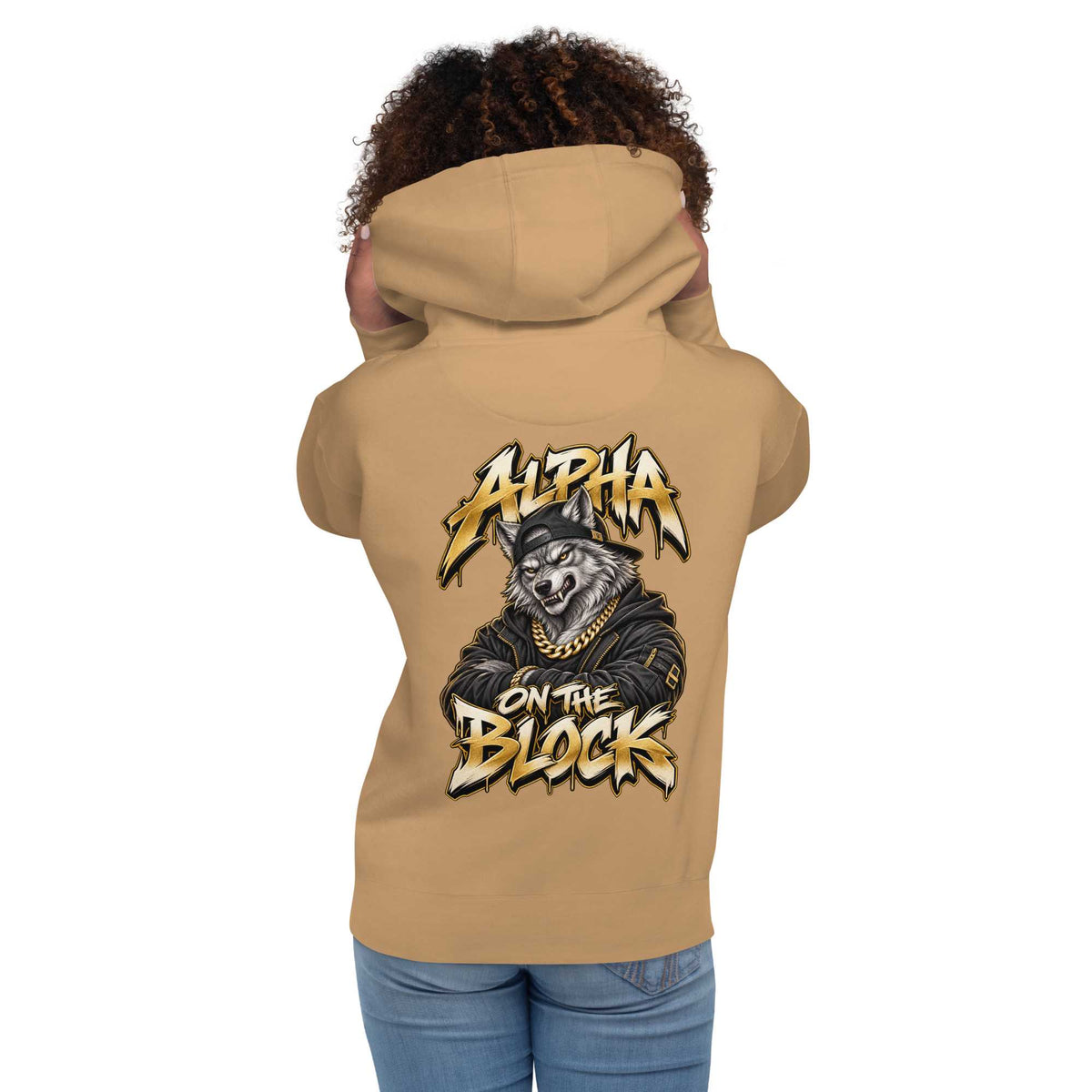 A woman shown from the back wearing a tan hoodie with a large  wolf graphic print on the back. The graphic features the text 'ALPHA ON THE BLOCK' in a stylized yellow and black font around an illustration of a wolf wearing a cap and gold chain.