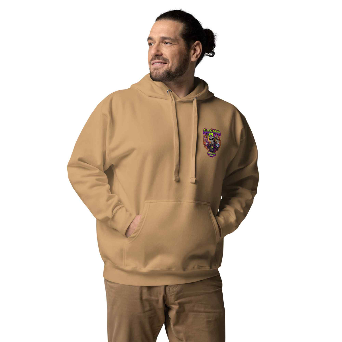 A man wearing a khaki color pullover hoodie with a colorful 'alien mob logo graphic on the left chest, paired with brown pants, set against a plain white background.