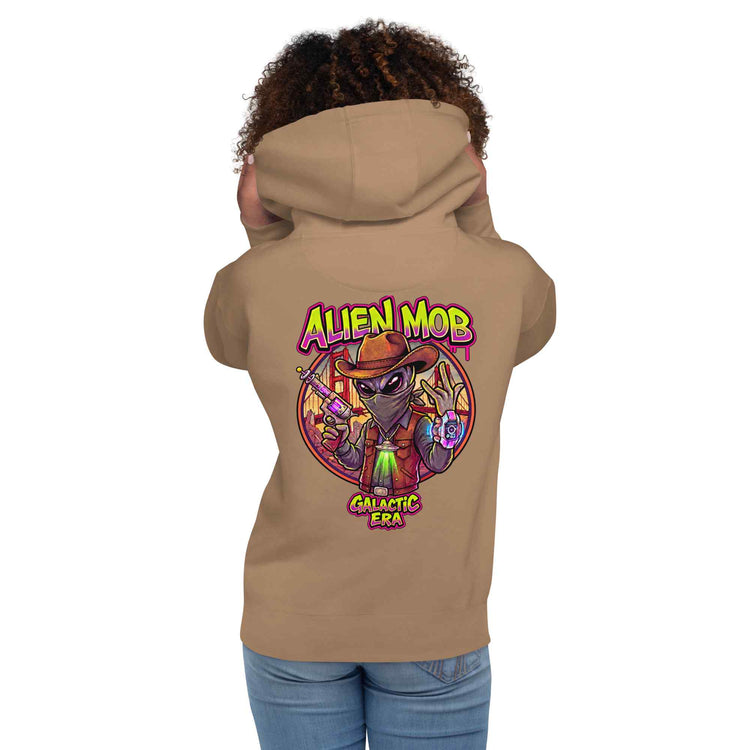 woman wearing a latte hoodie with alien mob cowboy outlaw  on the back of the hoodie paired with blue jeans on a white background back view