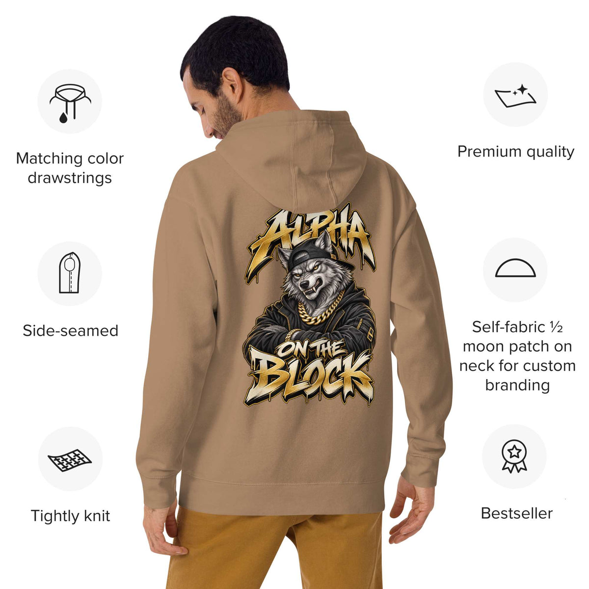 A man shown from the back wearing a tan hoodie with a large graphic Alpha On The Block print of a wolf wearing a gold chain and the text 'Alpha on the Block'. The image includes feature callouts on both sides highlighting details like matching color drawstrings, side-seaming, and a moon patch on the neck.