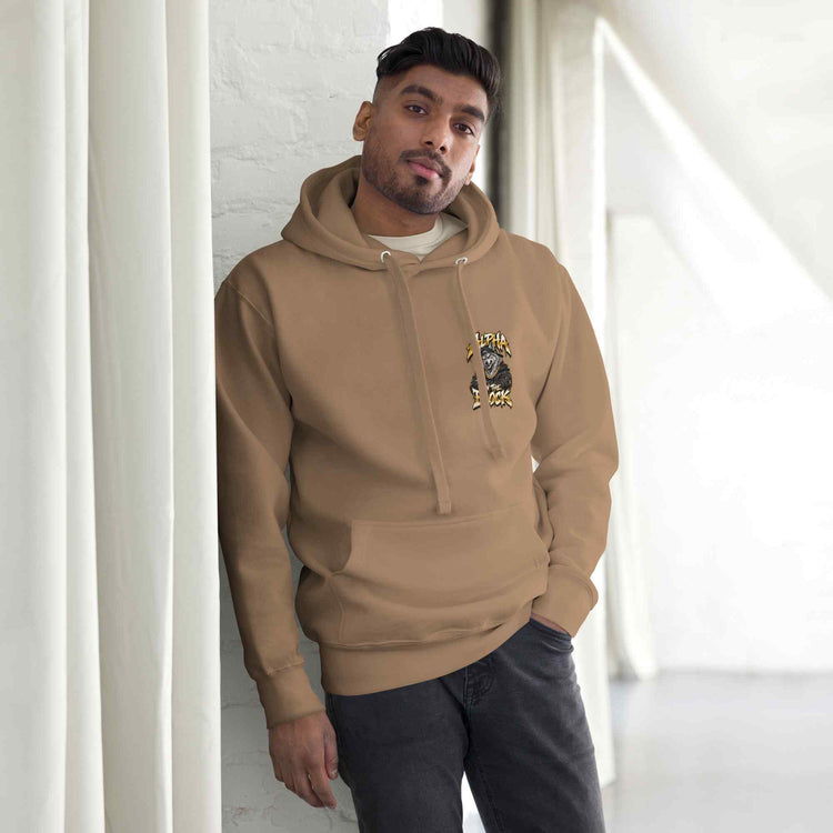 A man wearing a tan hoodie with a graphic print on the left chest, standing in a bright indoor setting with white curtains.