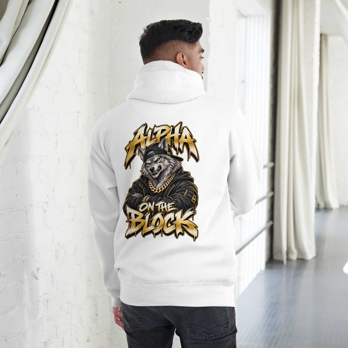 A man viewed from behind wearing a white hoodie with a large graphic print on the back. The graphic features a wolf wearing a cap and gold chain, with the text 'ALPHA ON THE BLOCK' in a stylized gold and black font.