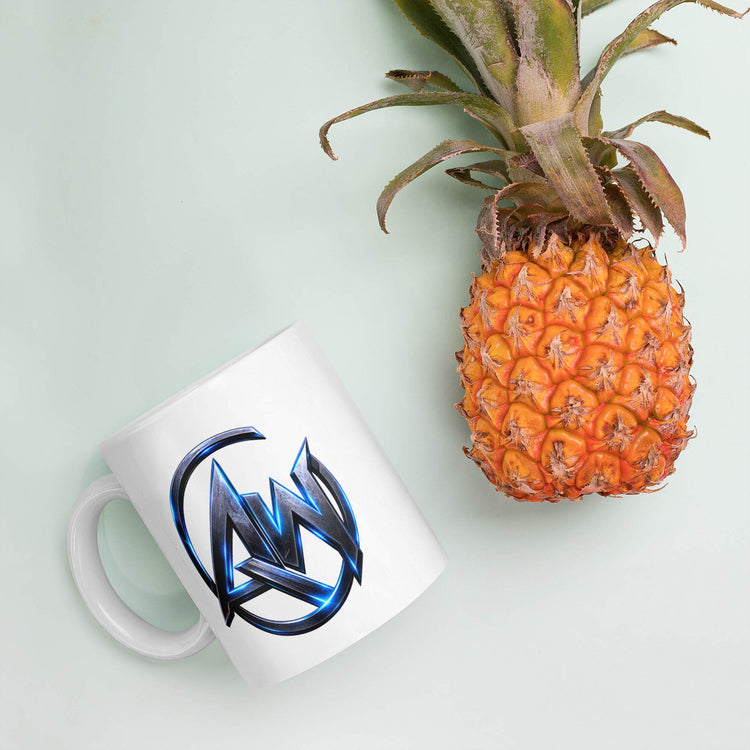 A white ceramic mug with a blue and black stylized 'AW' logo, styled next to a whole pineapple on a pale mint green background.