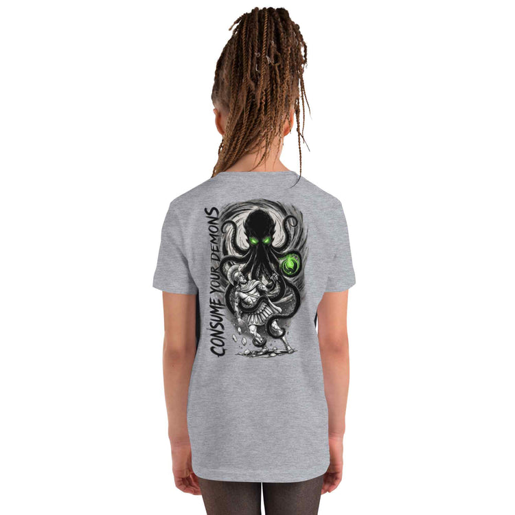 A girl with long brown dreadlocks is shown from the back wearing a heather gray t-shirt with a large graphic of a black octopus with green eyes and the text 'CONSUME YOUR DEMONS' printed on the back.