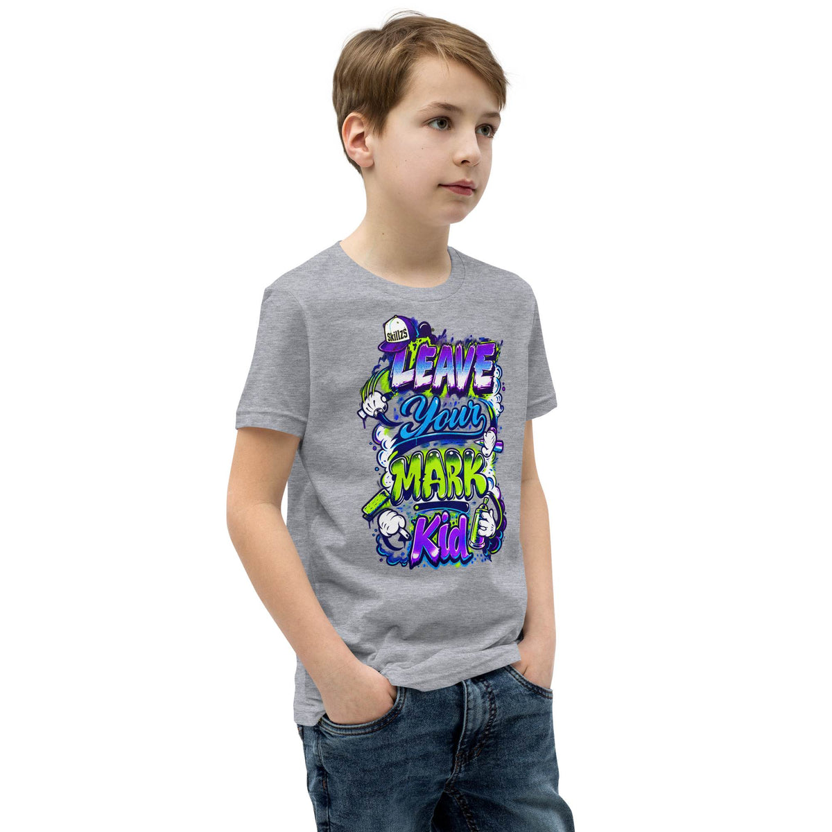 A child wearing a heather gray graphic t-shirt with a colorful cartoon design that reads 'LEAVE YOUR MARK Kid!'. The child is also wearing blue jeans, standing against a plain white background.