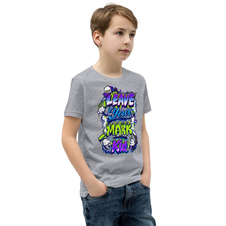 A child wearing a heather gray graphic t-shirt with a colorful cartoon design that reads 'LEAVE YOUR MARK Kid!'. The child is also wearing blue jeans, standing against a plain white background.