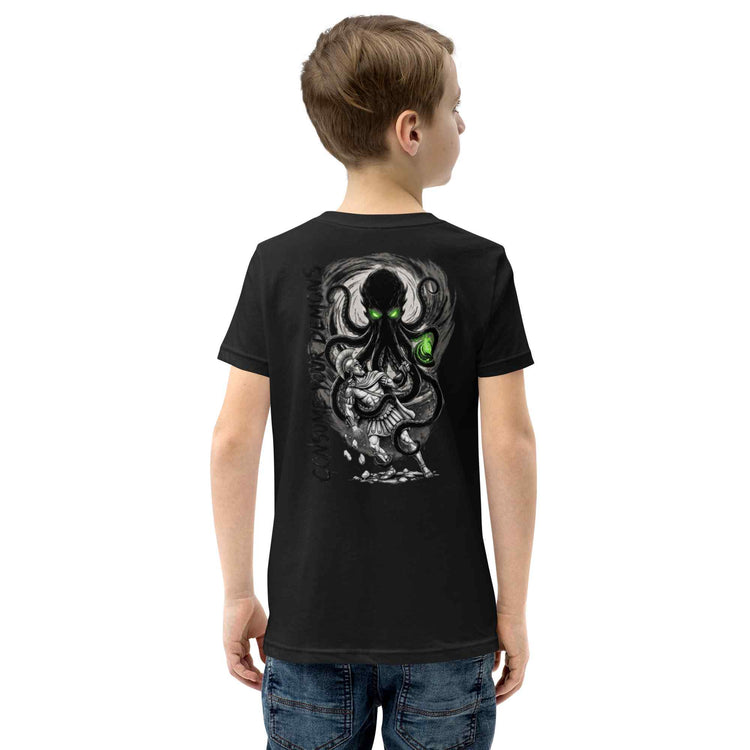 A child viewed from the back wearing a black short-sleeve T-shirt with a large kraken monster graphic and a bright green glowing eye on the back, paired with blue jeans against a plain white background.