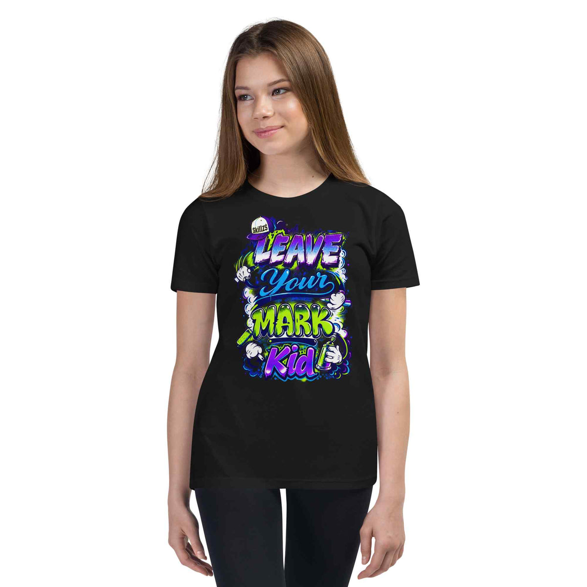 A young woman modeling a black short-sleeve t-shirt with a colorful graphic on the front that reads 'LEAVE YOUR MARK Kid' in purple, blue, and green lettering with cartoon characters.