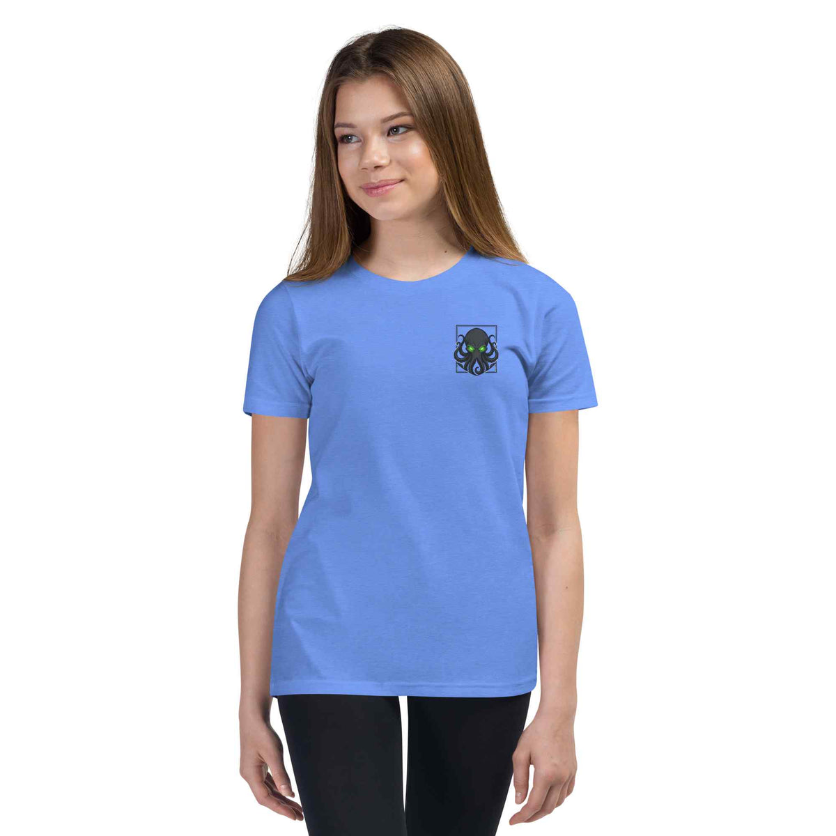 A young woman modeling a light blue crewneck t-shirt with a small dark graphic  kraken on the left chest, set against a plain white background.