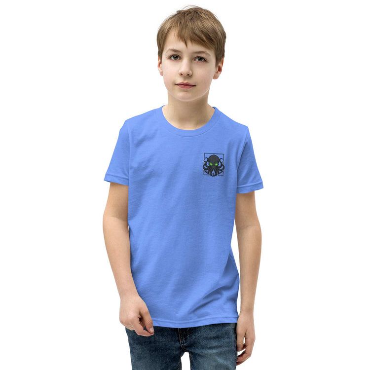 A young boy wearing a light blue crewneck t-shirt with a small kraken graphic on the left chest, paired with dark blue jeans, set against a plain white background.