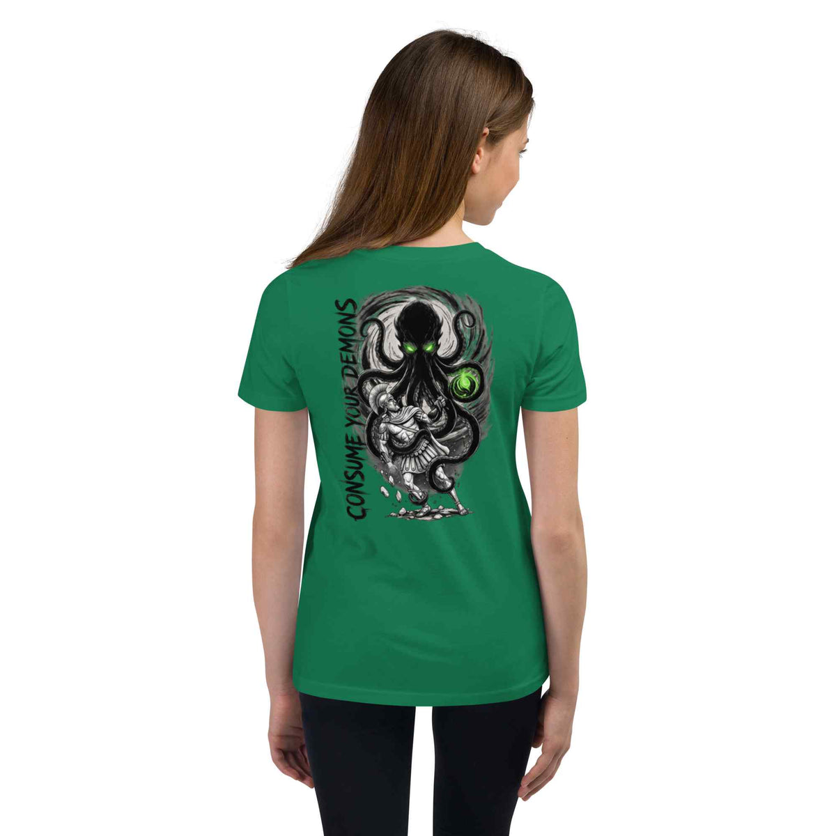 A woman viewed from the back wearing a green short-sleeve T-shirt with a large black and gray graphic of a multi-eyed monster and the text 'CONSUME YOUR DEMONS' printed vertically on the back.