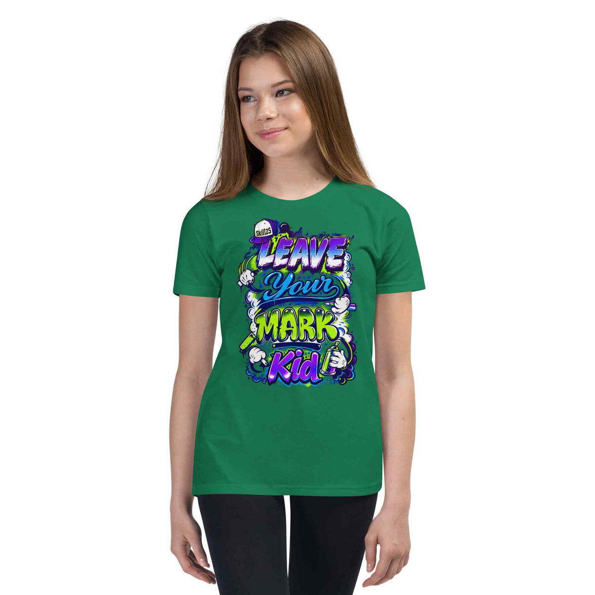A young woman modeling a green short-sleeve t-shirt with a colorful graphic that reads 'LEAVE YOUR MARK Kid' in purple, yellow, and white stylized lettering, set against a plain white background.