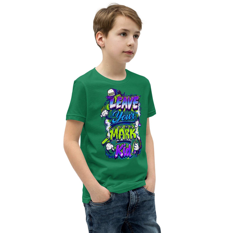 A young boy wearing a green graphic t-shirt with the text 'LEAVE YOUR MARK KID!' in colorful bubble letters, paired with blue jeans, set against a plain white background.