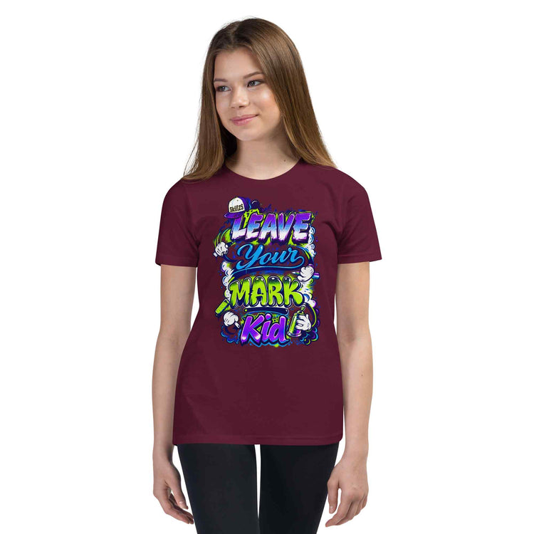 A young woman modeling a maroon short-sleeve t-shirt with a colorful graphic that reads 'LEAVE YOUR MARK Kid' in stylized purple, green, and white lettering, set against a plain white background.